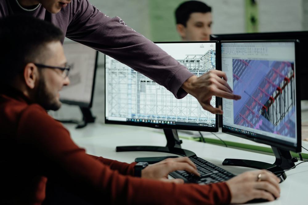 Two designers reviewing a technical drawing and a 3D model on computer screens