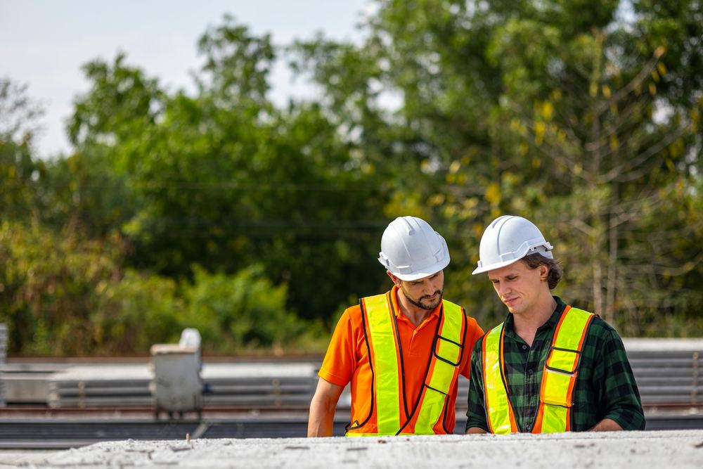 Two people in hi-vis vests and hard hats looking over plans on an outdoor site